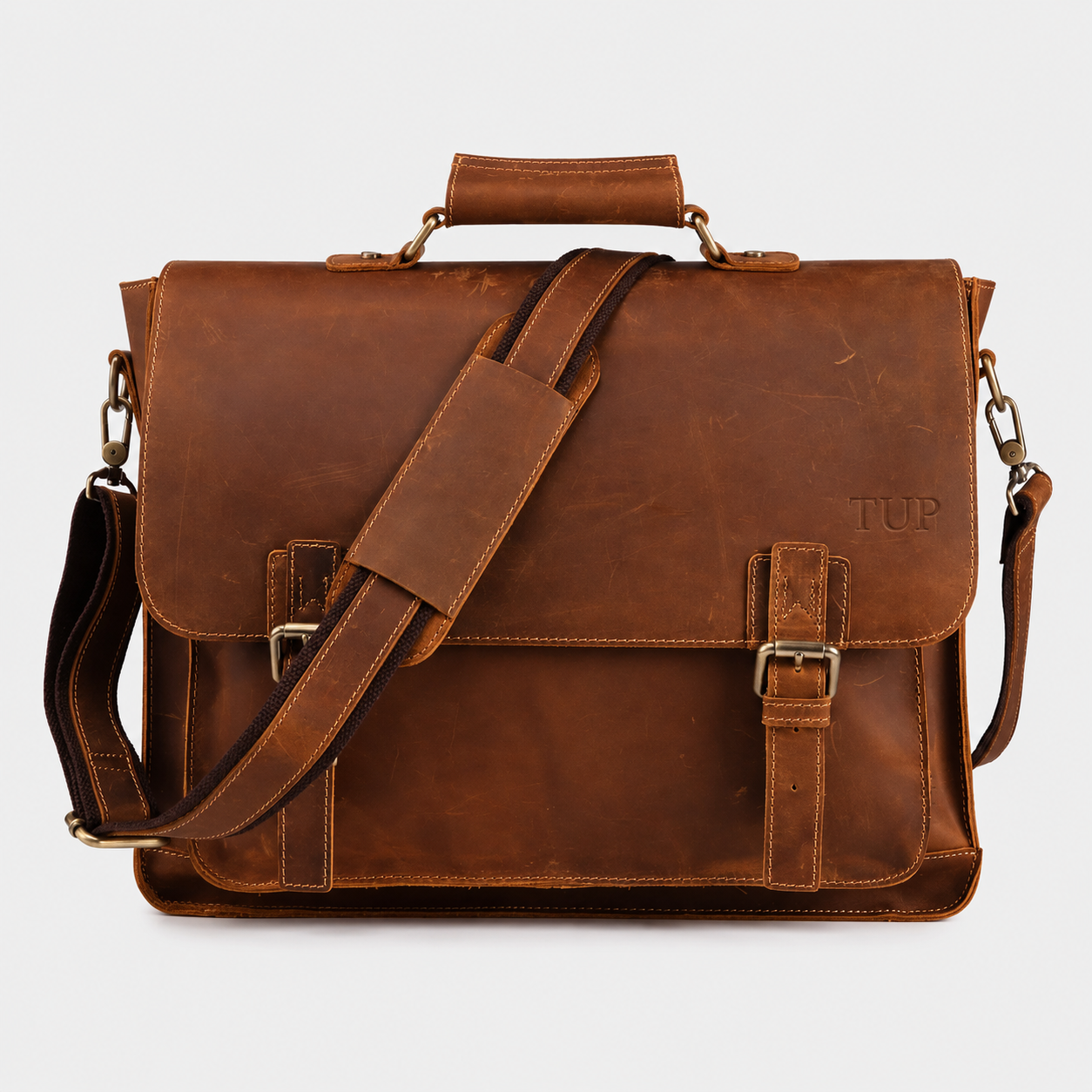 A brown leather briefcase with a top handle, adjustable shoulder strap, and buckle closures, featuring the monogram 'TUP' on the front, set against a light gray background.