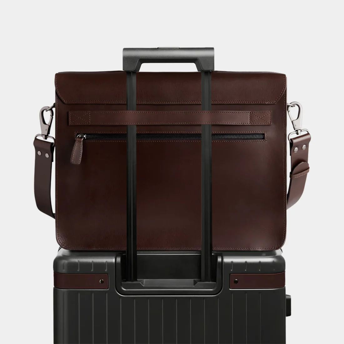 Leather briefcase attached securely to rolling luggage using rear luggage strap for travel convenience.